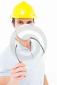 Worker wearing mask and hardhat while holding protective glasses