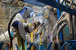 Worker wearing protective equipment welding a chassis in car factory photo