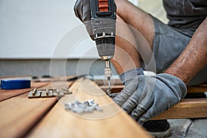 Worker wearing protective gloves fixating wooden plank for outside patio