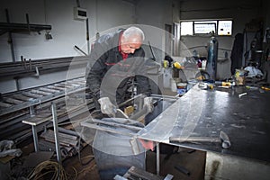 A Worker, welder in work clothes, construction gloves and a welding mask is welded with a welding machine metal product table,