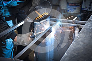 A Worker, welder in work clothes, construction gloves and a welding mask is welded with a welding machine metal product table,