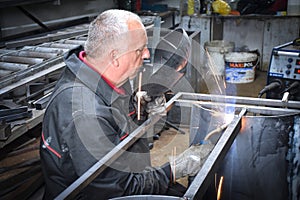 A Worker, welder in work clothes, construction gloves and a welding mask is welded with a welding machine metal product table,