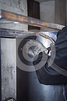 A Worker, welder in work clothes, construction gloves and a welding mask is welded with a welding machine metal product table,