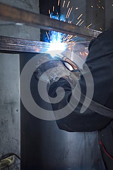 A Worker, welder in work clothes, construction gloves and a welding mask is welded with a welding machine metal product table,