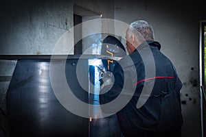 A Worker, welder in work clothes, construction gloves and a welding mask is welded with a welding machine metal product table,