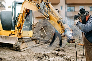 worker welding broken excavator on construction site