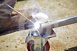 Worker with a welding machine fixing a caster wheels, fiery sparks flying around
