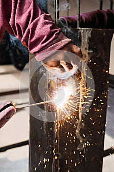 Worker welding steel with spark lighting and smoke at construction site