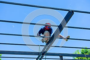 Worker welding the steel structure of roof with arc welding machine and blue sky in background