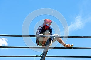 Worker welding the steel structure of roof with arc welding machine and blue sky in background