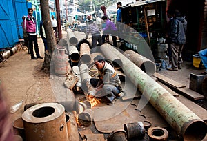 Worker welds metal pipe near a warehouse of steel