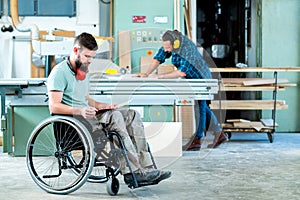 Worker in wheelchair in a carpenter`s workshop with his colleagu