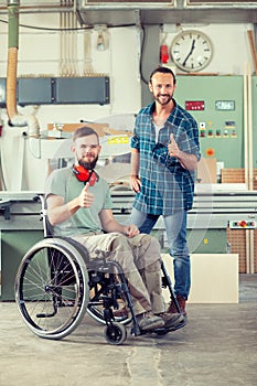 Worker in wheelchair in a carpenter`s workshop with his colleagu