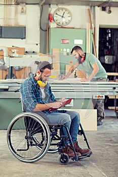 Worker in wheelchair in a carpenter`s workshop with his colleagu