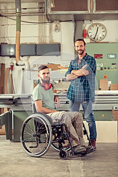 Worker in wheelchair in a carpenter`s workshop with his colleagu