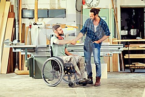 Worker in wheelchair in a carpenter`s workshop with his colleagu