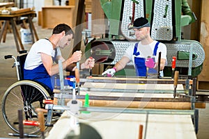 Worker in wheelchair in a carpenter's workshop with his colleagu