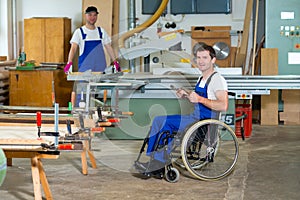 Worker in wheelchair in a carpenter's workshop with his colleagu