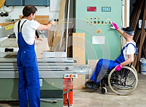 Worker in wheelchair in a carpenter's workshop with his colleagu