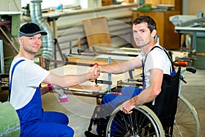 Worker in wheelchair in a carpenter's workshop with his colleagu