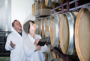 Worker of winery holds glass of red wine in hand and shows him to expert