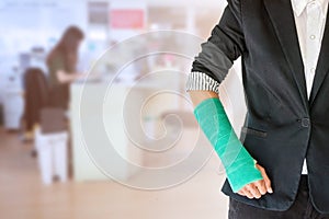 worker woman accident on arm with green arm cast on blurred business office working space background