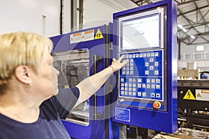 A worker woman presses a button and starts an automatic manufacturing process in a factory