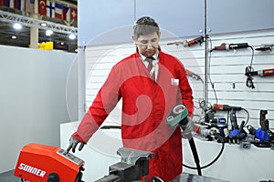 Worker in work clothes and protective glasses switching the control panel on to sand metal sheet by the hand held pneumatic belt
