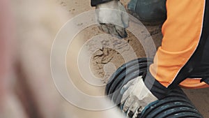 Worker in work gloves rubber boots pull sand out black plastic pipe