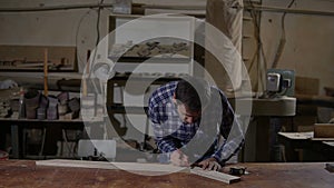 Worker in work shirt measures wooden board with long yellow ruler on a workbench