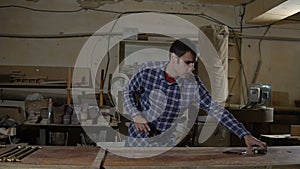 Worker in work shirt measures wooden board with long yellow ruler on a workbench