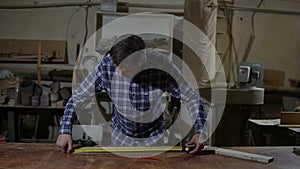 Worker in work shirt measures wooden board with long yellow ruler on a workbench