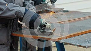 Worker on workbench processes iron sheets with grinding tool and sparks fly. Close-up video. Authentic workflow.