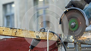 Worker working with angle grinder. Electric wheel grinding on steel structure. Sparks. Defocused background.