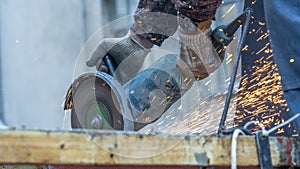 Worker working with angle grinder. Electric wheel grinding on steel structure. Sparks. Defocused foreground