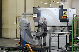 a worker working in a modern industry prepares material for processing on a cnc machine, wears a protective mask on his