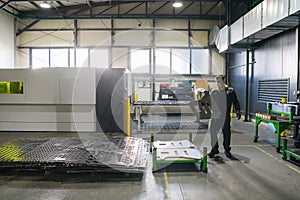 a worker working in a modern industry prepares material for processing on a cnc machine, wears a protective mask on his