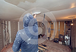 Worker is working with palette-knife for flattening the ceiling from wooden platform in room of apartment is inder