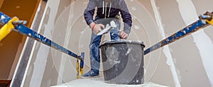 Worker is working with palette-knife for flattening the ceiling from wooden platform in room of apartment is inder