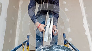 Worker is working with palette-knife for flattening the ceiling from wooden platform in room of apartment is inder