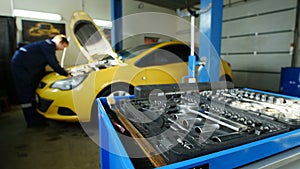 Worker works in professional car workshop near yellow car, time-lapse