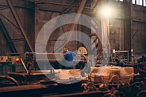 Worker in workshop processes large cast iron part after casting in metallurgical foundry plant