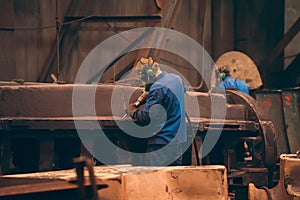 Worker in workshop processes large cast iron part after casting in metallurgical foundry plant