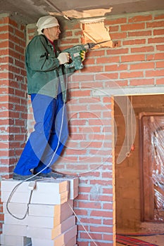 The worker in workwear makes a hole in the wall