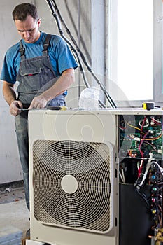 A worker in workwear sets air conditioner in the