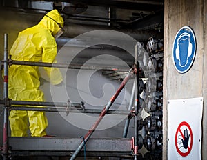 Worker in a yellow plastic overall is busy with high pressure cleaning a heat exchanger