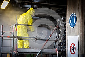 Worker in a yellow plastic overall is busy with high pressure cleaning a heat exchanger