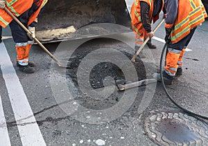 The workers` brigade clears a part of the asphalt with shovels in road construction