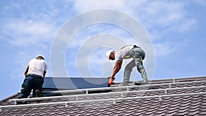 Workers building solar panel system on roof of house. Installers carrying photovoltaic solar module