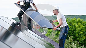 Workers building solar panel system on roof of house. Installers carrying photovoltaic solar module